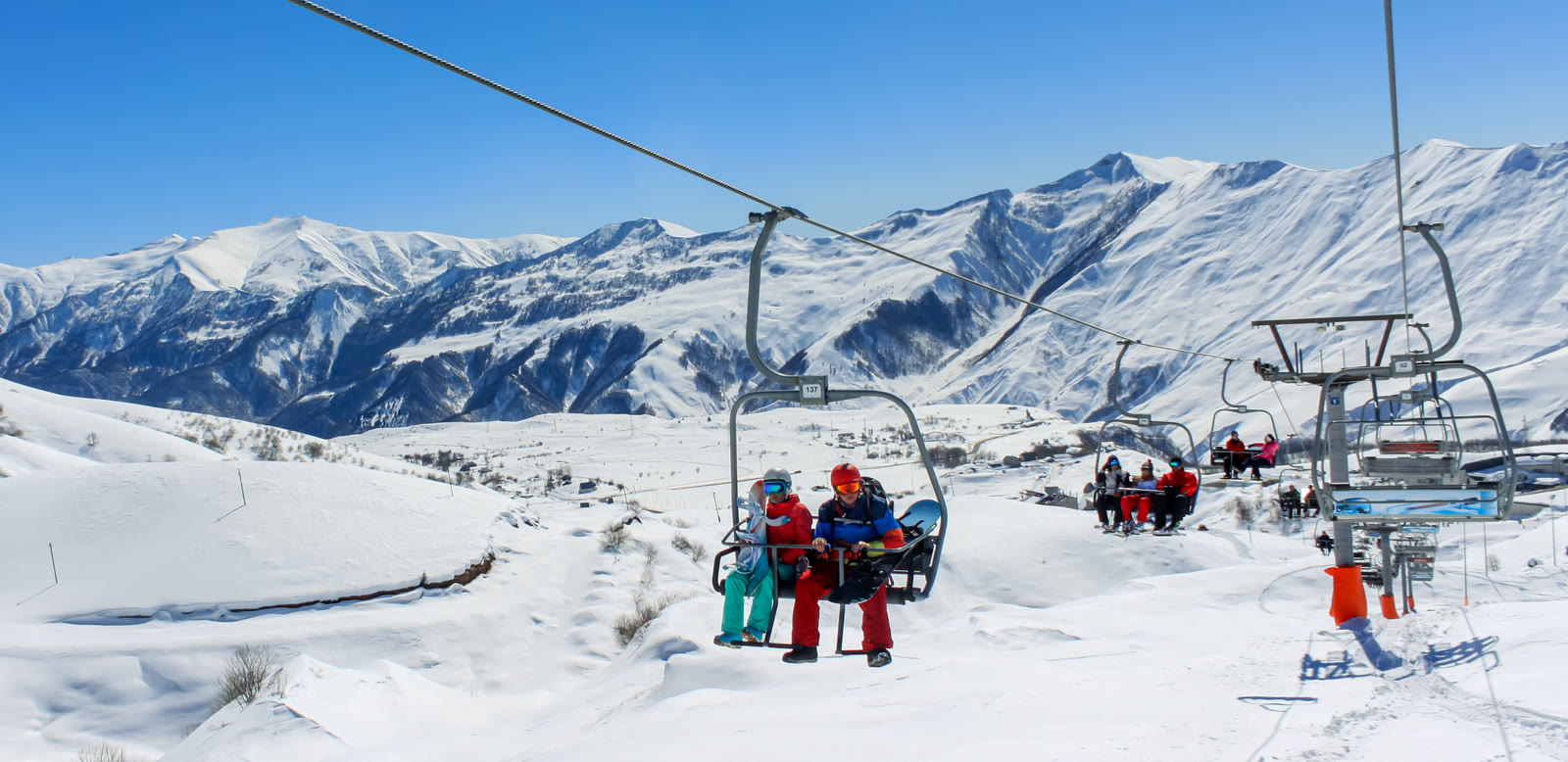 Skiers riding a chairlift above snowy slopes on a sunny day