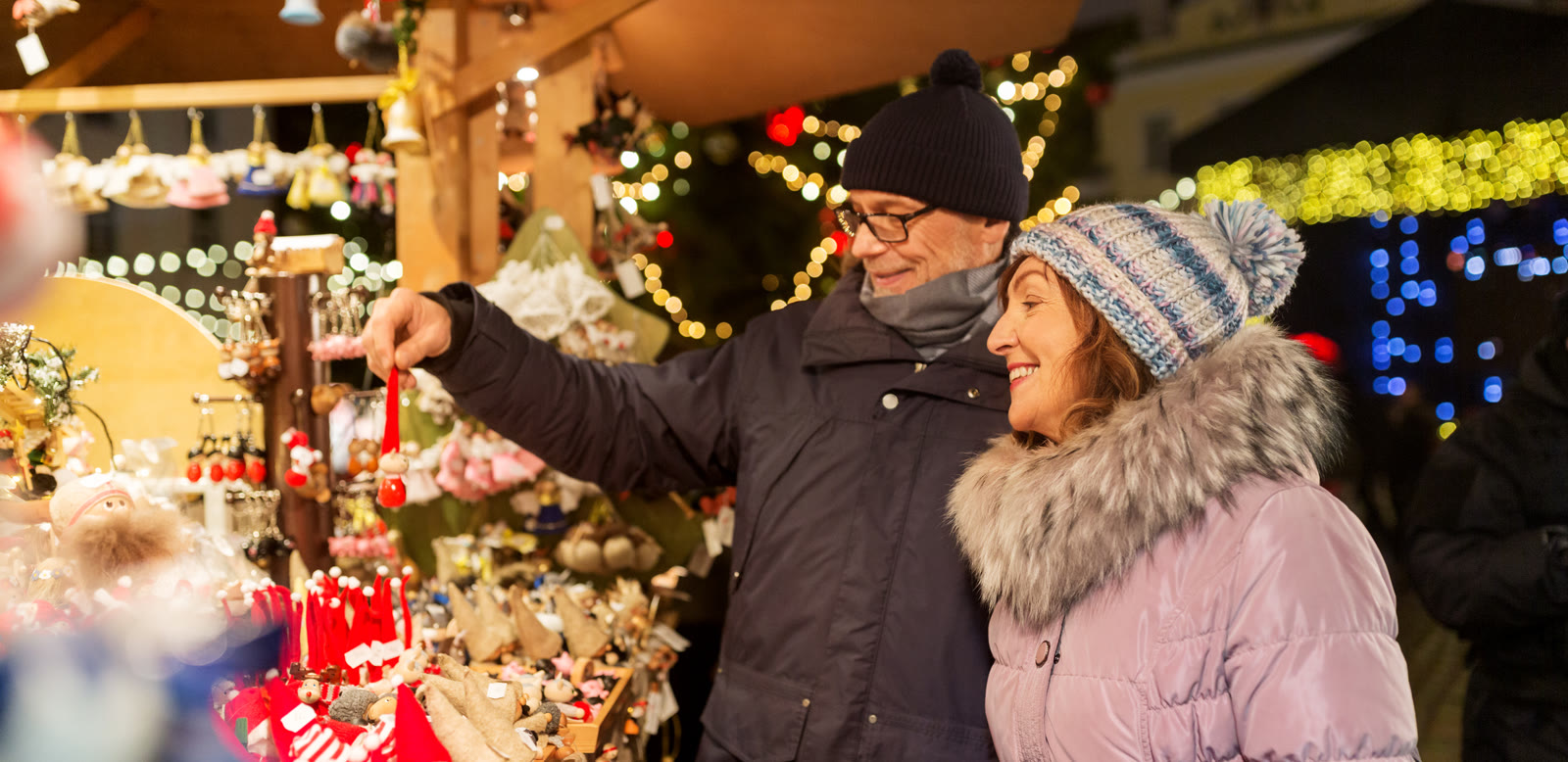 A couple browsing ornaments at a lit-up Christmas market stall