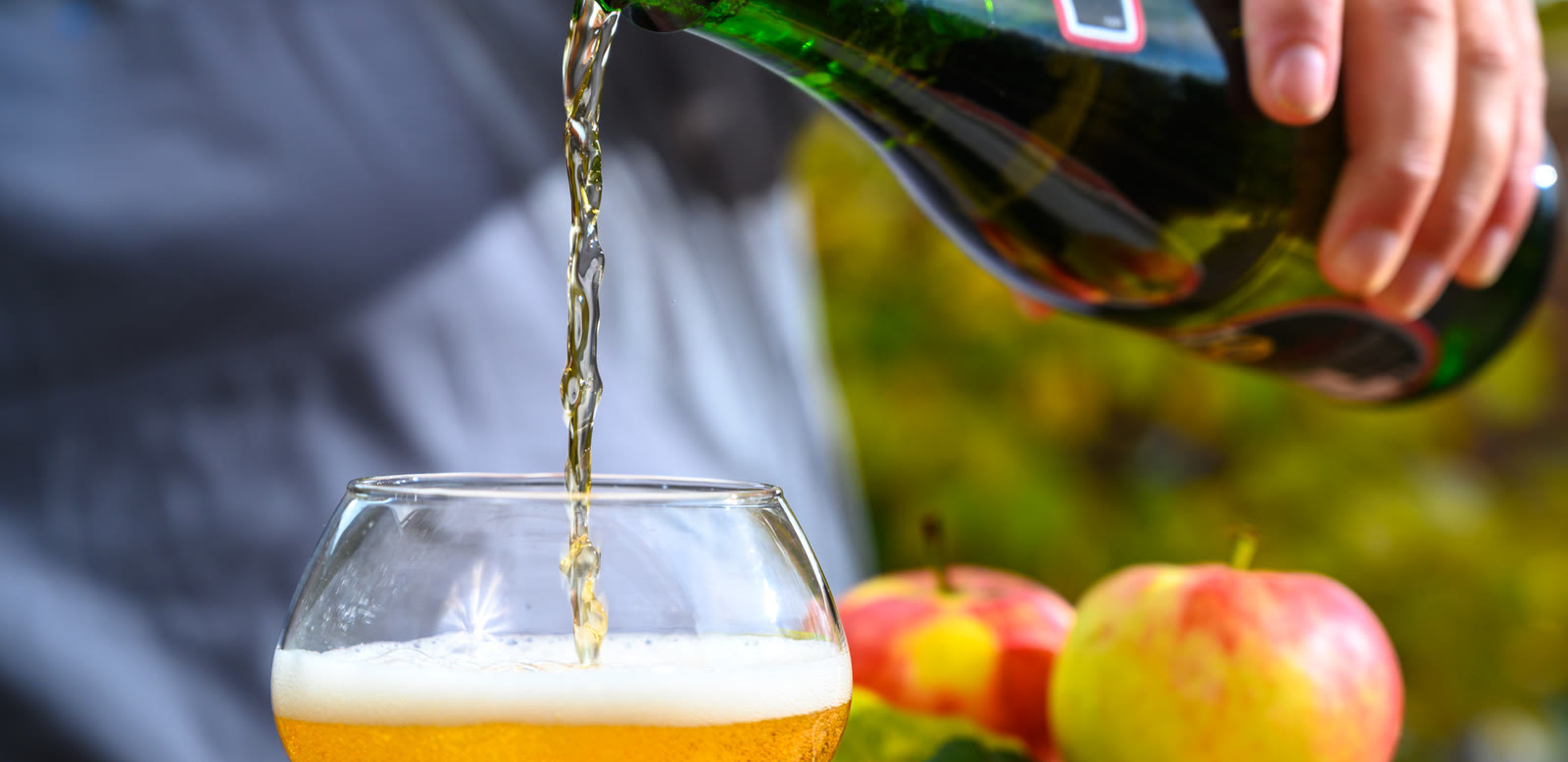 Apple cider poured into a glass in an orchard at harvest