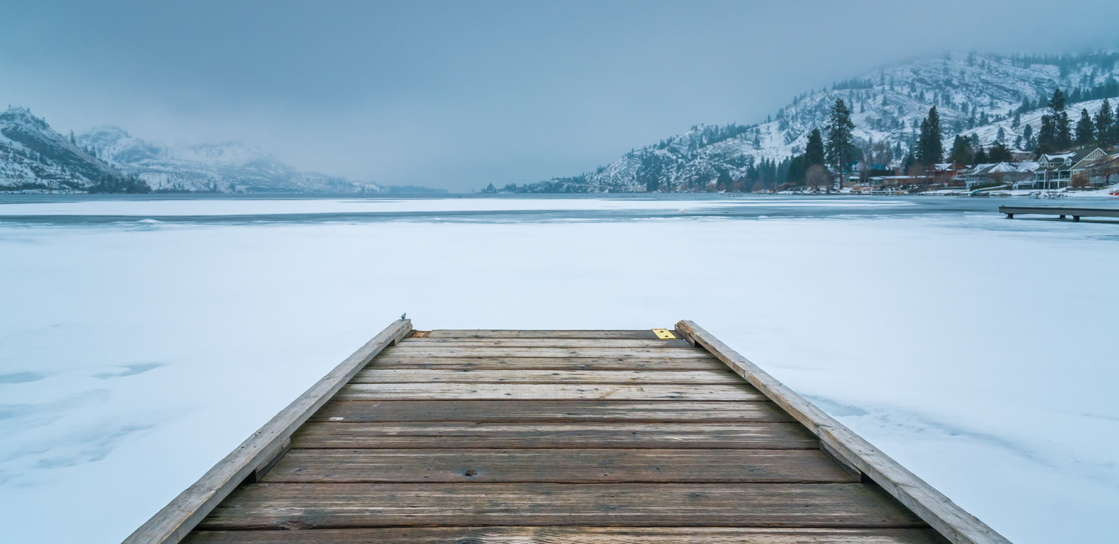 A wooden dock on a frozen lake with snowy mountains behind