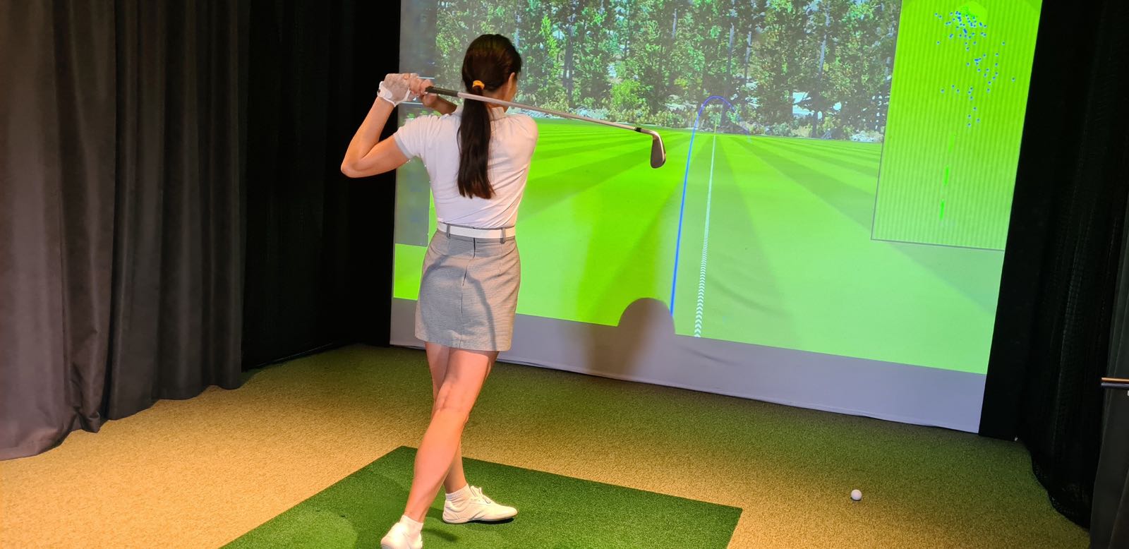 A golfer mid-swing in an indoor golf simulator bay