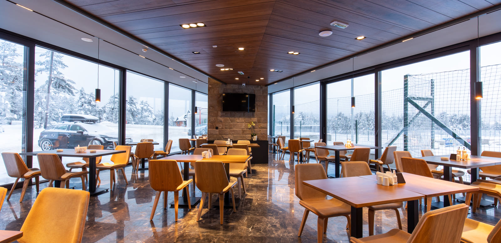 A mountain restaurant with a fireplace and big windows onto the snow