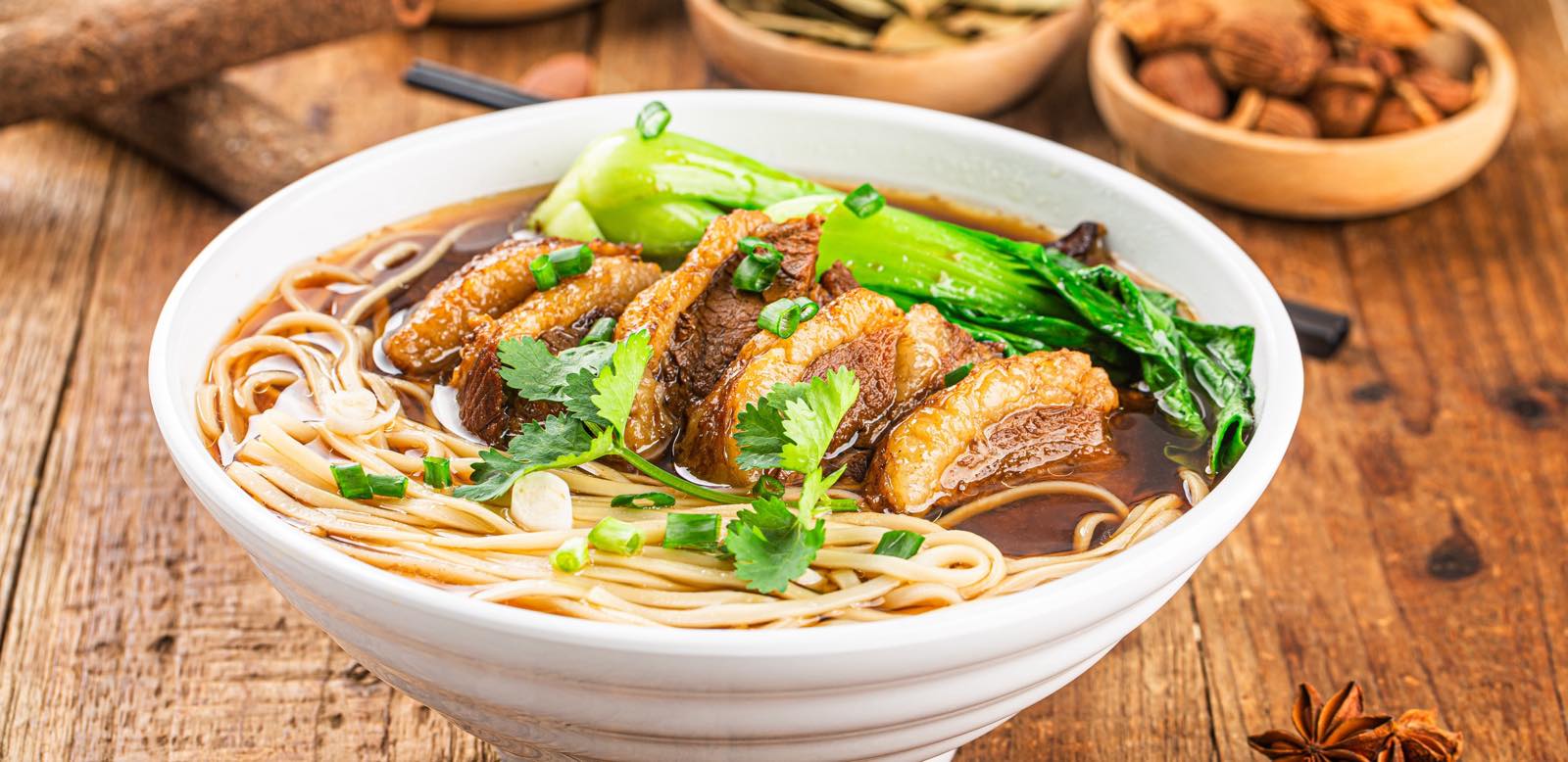 A steaming bowl of beef noodle soup on a wooden table