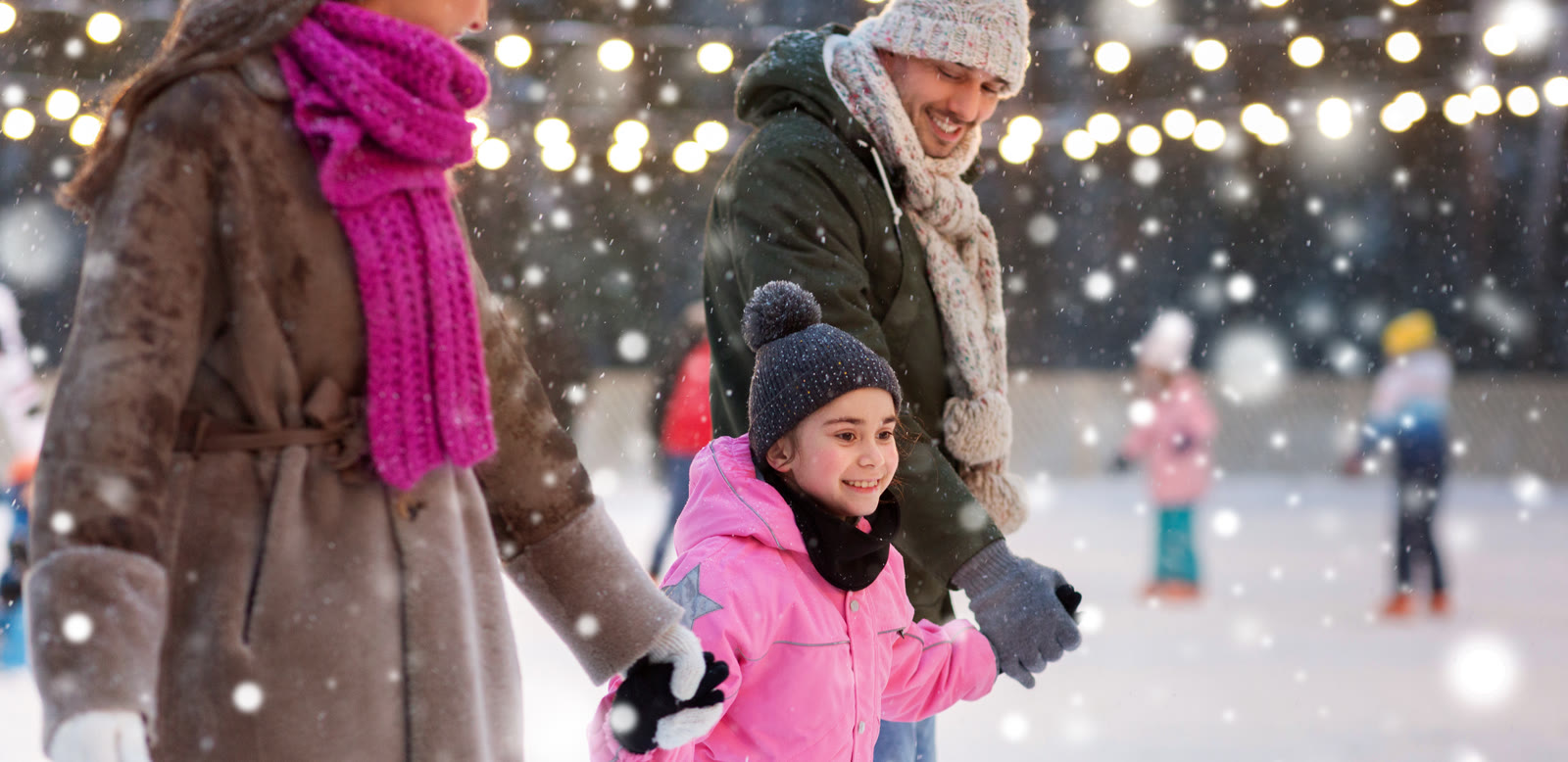 A family skating together on an outdoor rink in falling snow