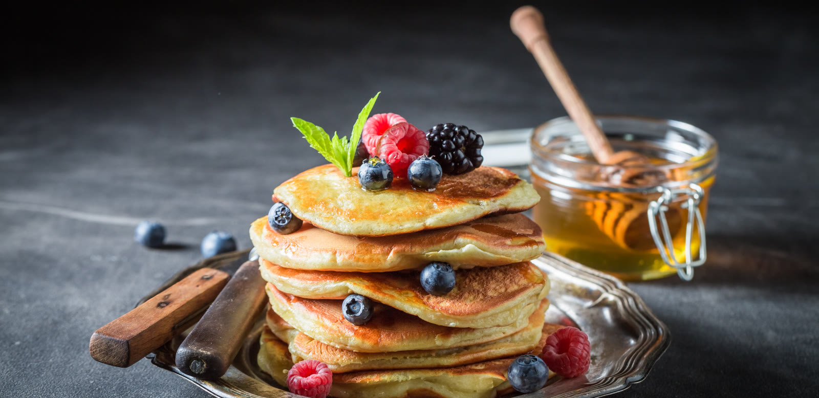 A stack of pancakes topped with fresh berries, with a jar of honey