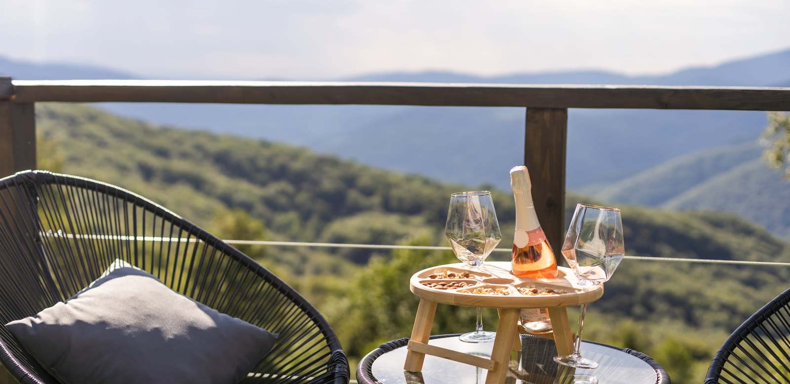 Wine glasses on a patio table overlooking forested hills