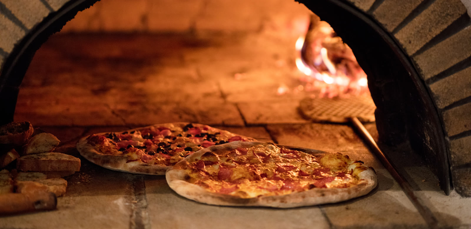 A pizza baking in a wood-fired brick oven