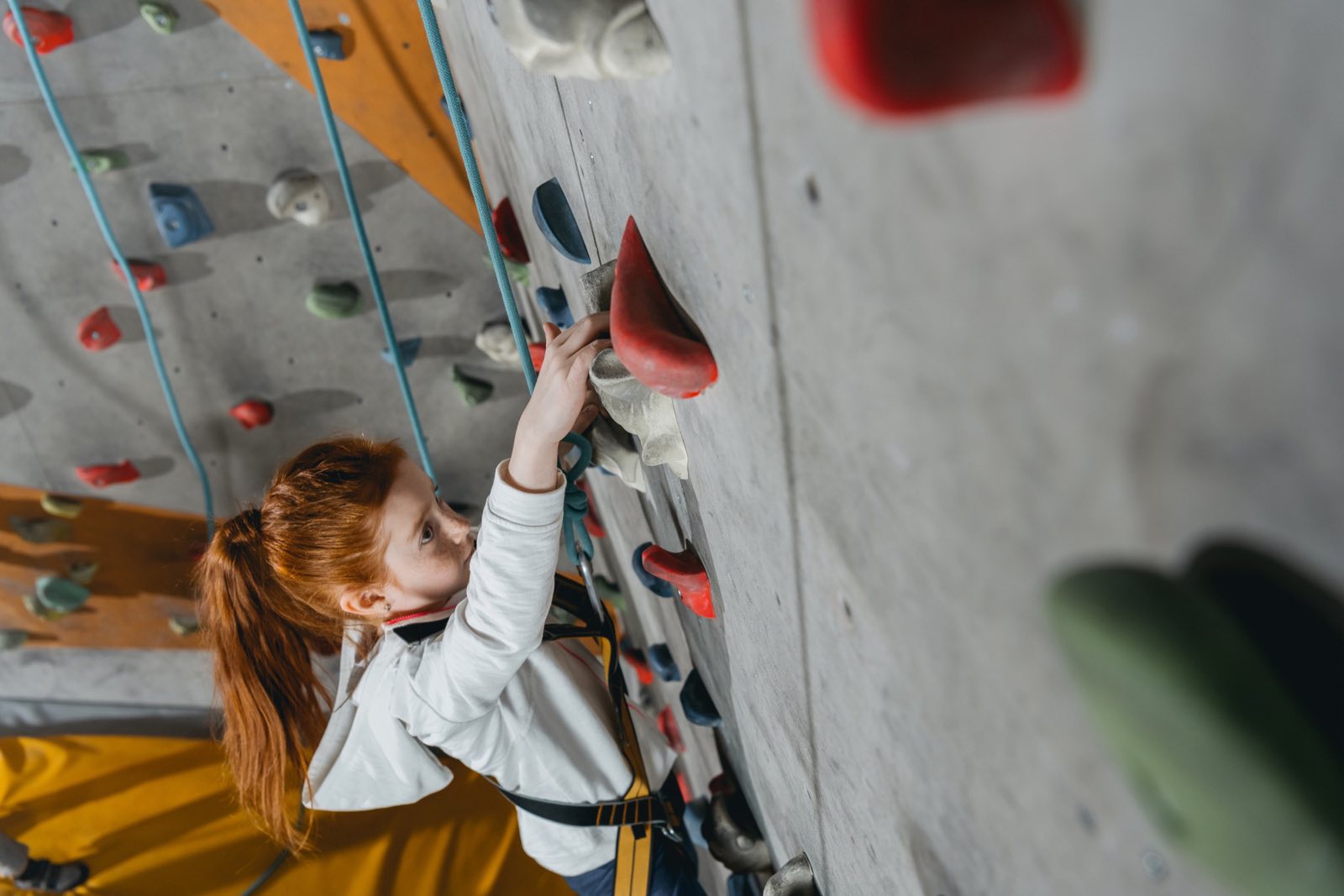 A girl reaching for a hold on an indoor climbing wall