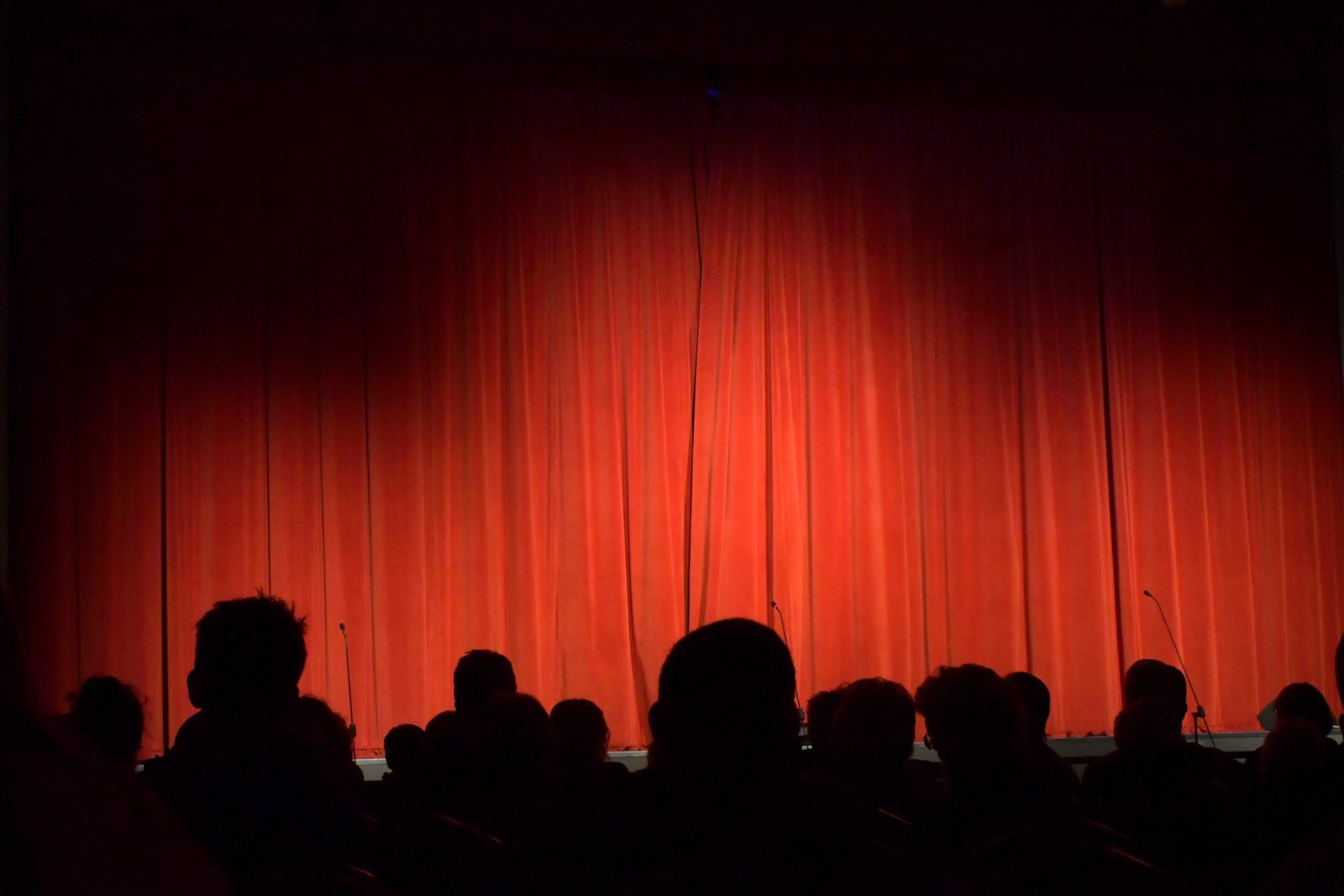 An audience waiting in front of a red stage curtain