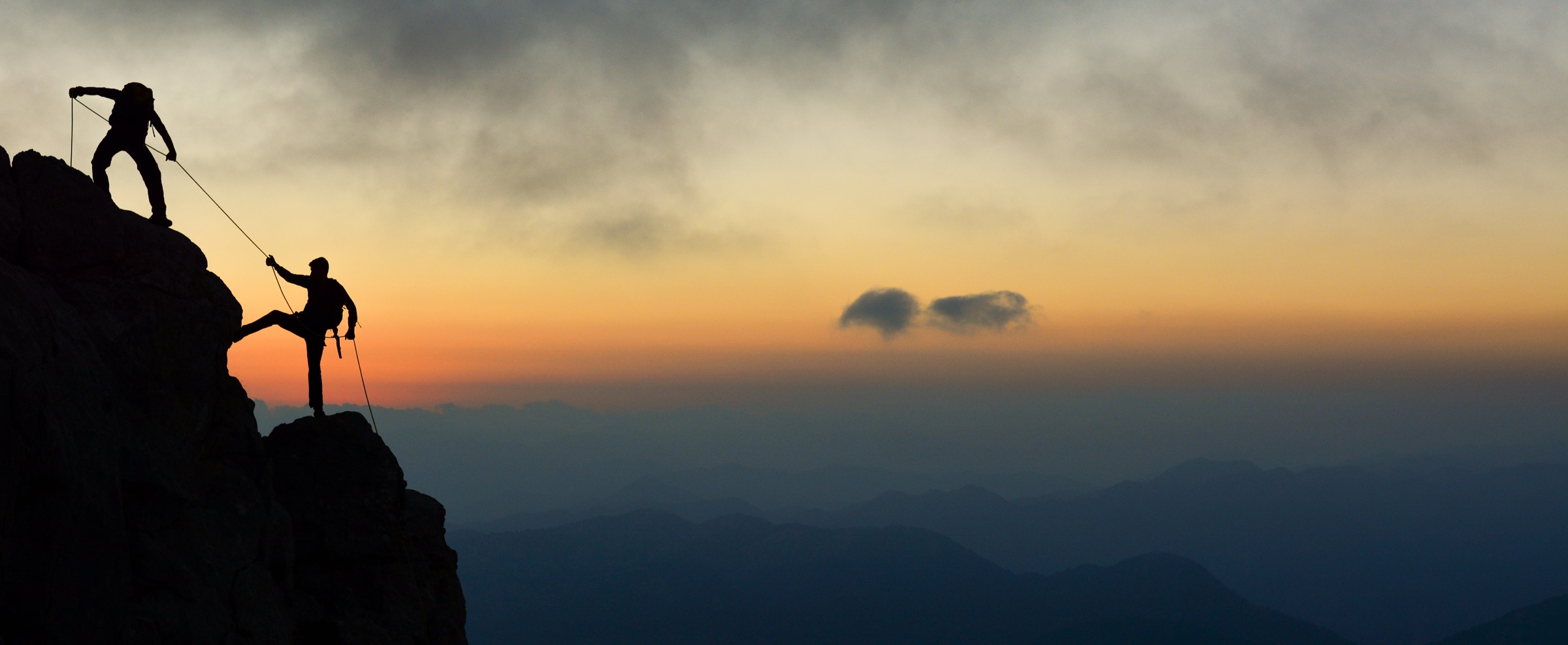 Deux grimpeurs encordés sur un sommet rocheux au coucher du soleil