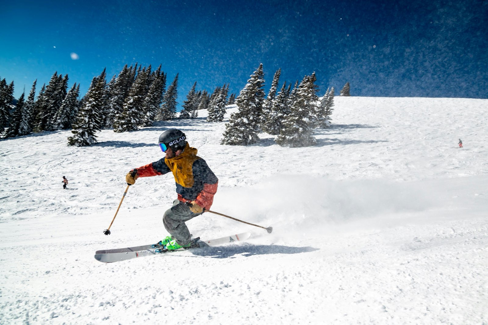 A skier carving past snow-covered fir trees under a blue sky
