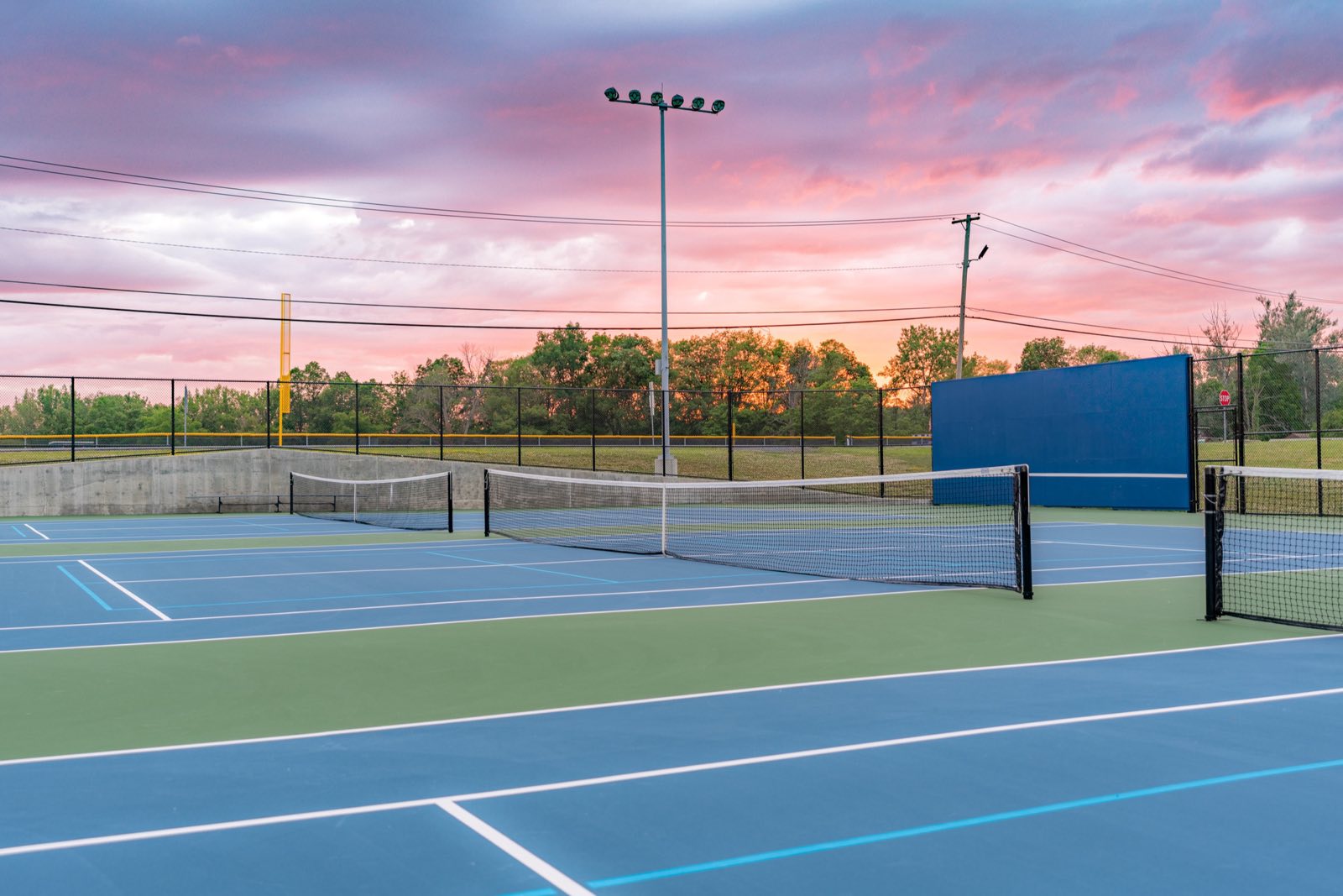 Outdoor tennis and pickleball courts under a pink evening sky