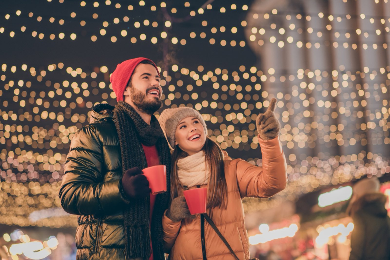 Two friends with warm drinks under holiday lights