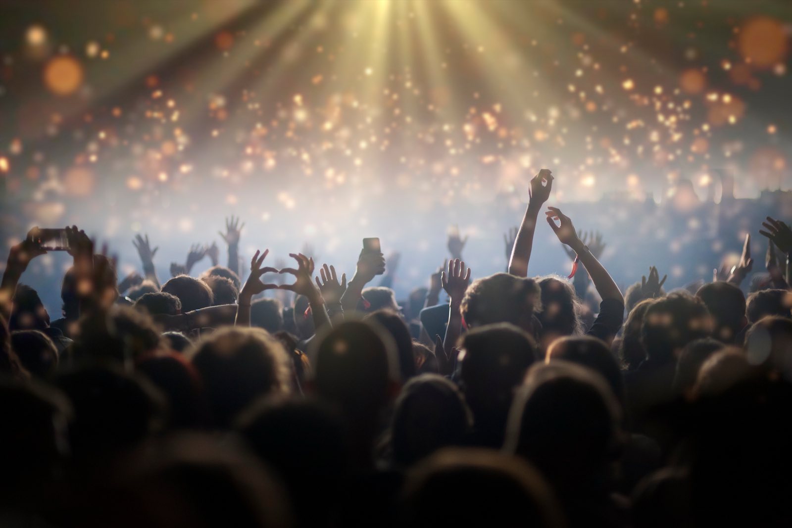 A festival crowd with hands raised under bright stage lights